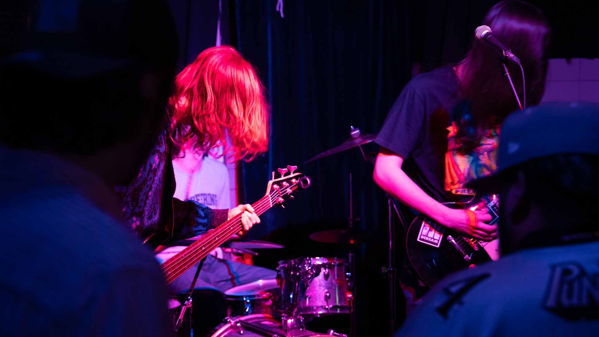 Two guitarists playing together under red and violet stage lights