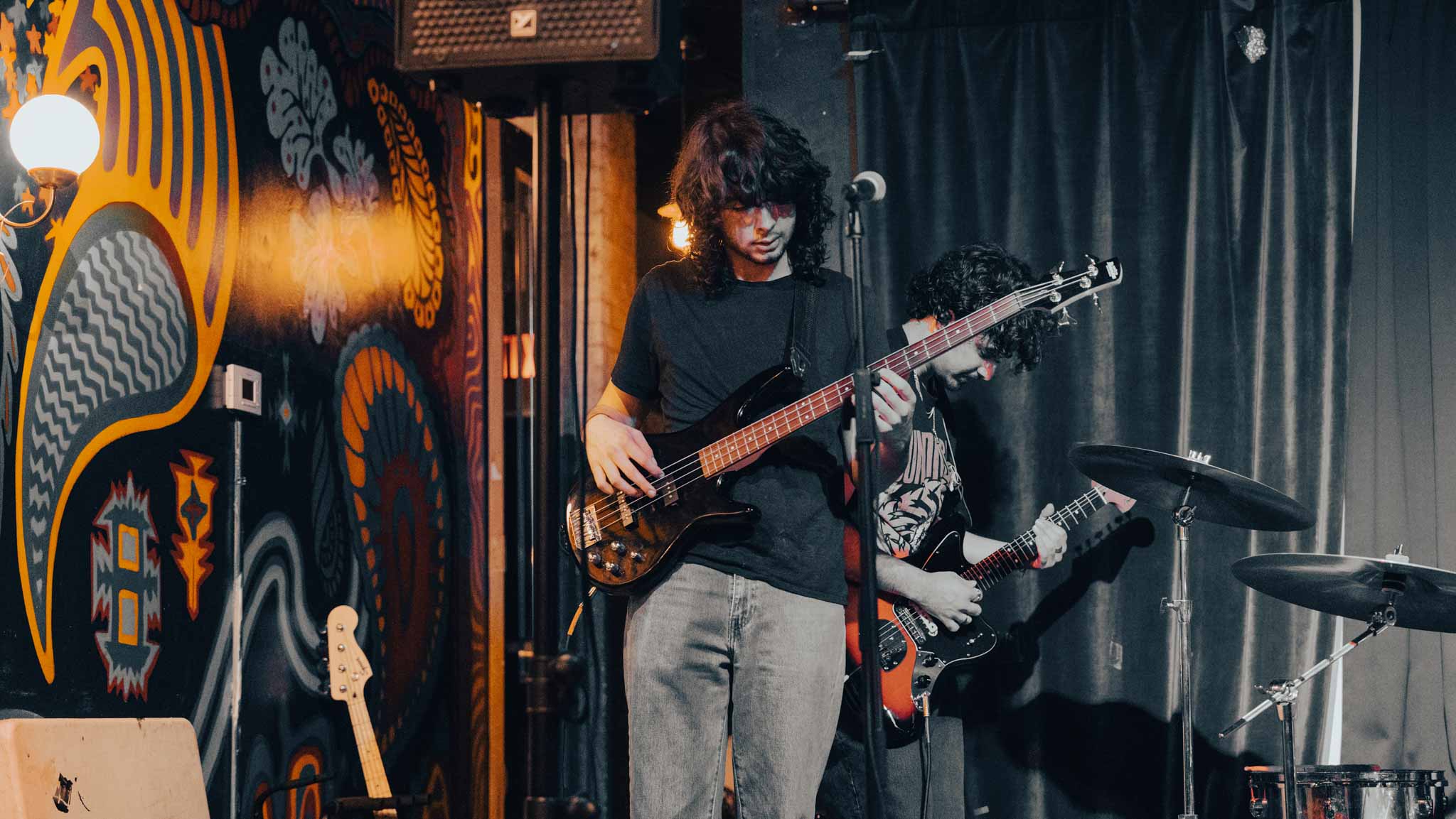 Bassist playing on a mural-lined stage with the guitarist and drummer behind