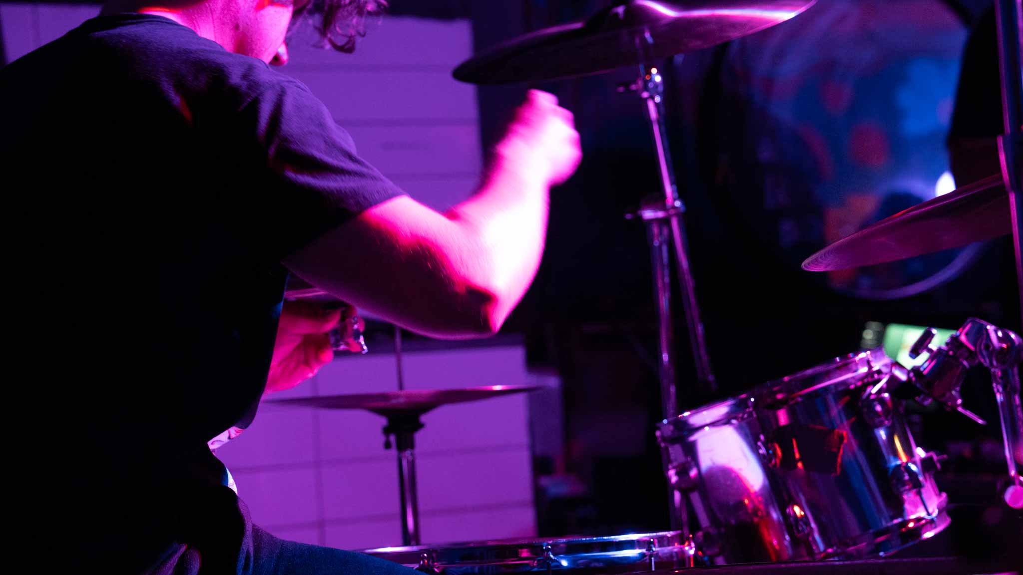 Drummer playing under magenta and blue stage lights